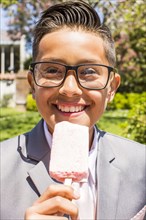 Smiling Hispanic boy wearing suit eating popsicle