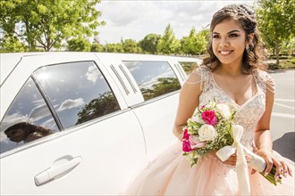 Hispanic girl wearing gown holding flowers near limousine