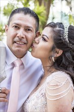 Hispanic girls wearing gown kissing father on cheek