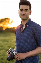 Smiling Chinese man holding camera in field