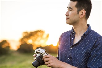 Smiling Chinese man holding camera in field