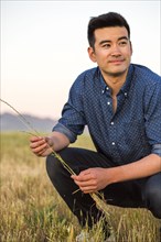 Smiling Chinese man crouching and holding grass in field
