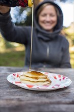 Smiling Caucasian woman pouring syrup on pancakes