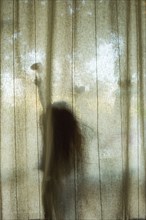 Silhouette of Caucasian girl touching heart-shape behind window curtain