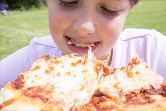 Close up of Caucasian girl with braces biting pizza
