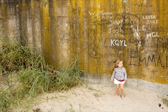 Caucasian girl standing in sand near graffiti wall
