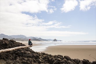 Caucasian woman sitting on log on rocks at beach