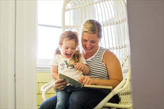 Caucasian mother reading book to excited daughter sitting on lap