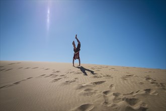 Caucasian teenage boy doing cartwheels on sand dune