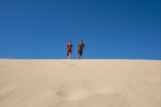 Caucasian father and son running on sand dune