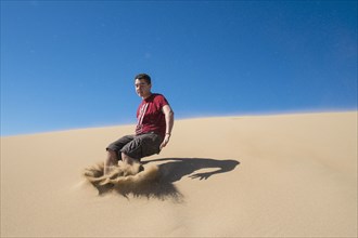Caucasian teenage boy jumping on sand dune
