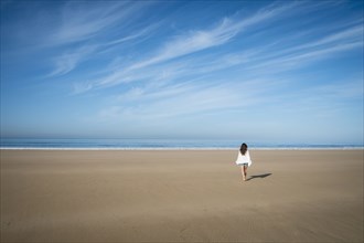 Caucasian woman walking on beach under blue sky