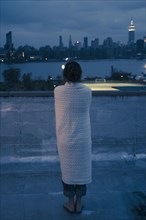 Caucasian woman wrapped in blanket admiring urban waterfront from rooftop