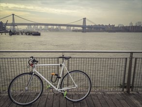 Bicycle locked to waterfront railing overlooking urban bridge
