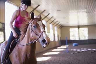 Caucasian woman riding horse in indoor paddock