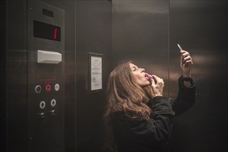 Caucasian woman applying lipstick in elevator