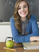Student with apple smiling at desk in classroom