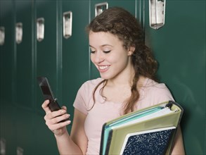 Mixed race student using cell phone by locker in school hallway