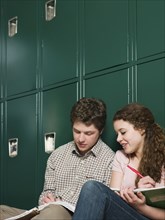 Students doing homework at locker in school hallway