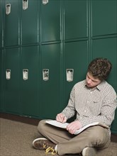 Student writing notes at locker in school hallway