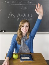 Student raising her hand at desk in classroom