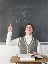 Student having idea under light bulb on chalkboard in classroom