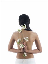 Rear view of nude woman holding flowers behind back