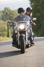 Older couple riding motorcycle on empty road