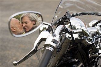 Older couple kissing in motorcycle side mirror reflection