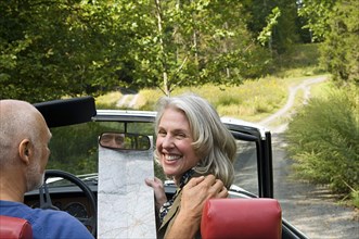 Older couple driving convertible on dirt road