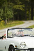 Older couple kissing in convertible on dirt road