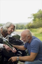 Older couple repairing motorcycle in park