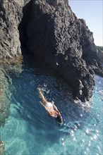 Woman swimming in ocean by rocky cliffs