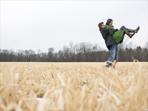 Caucasian man lifting girlfriend in rural field