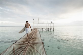 Surfer carrying surfboard on metal dock over ocean