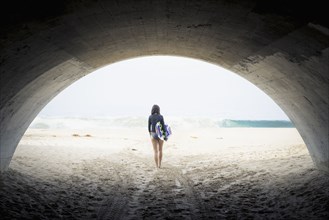 Caucasian woman carrying skimboard under arch
