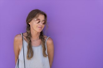 Caucasian woman wearing sunglasses leaning on purple wall