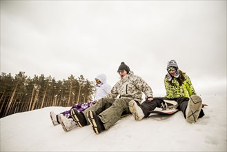 Caucasian friends sitting on snowboards