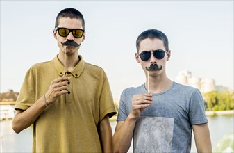 Caucasian men playing with fake mustaches in city