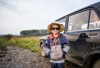 Caucasian boy standing near car in rural field
