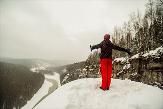 Caucasian hiker standing with arms outstretched on snowy hilltop
