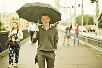 Caucasian man walking under umbrella on sidewalk