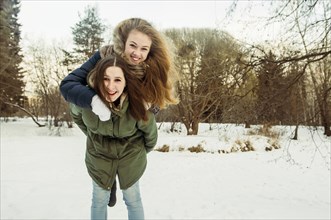 Caucasian woman carrying friend piggyback in snowy field