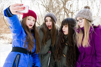 Caucasian girls taking cell phone photograph in snowy field