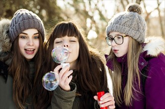 Caucasian girls blowing bubbles outdoors in winter
