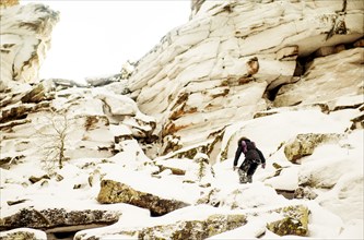 Caucasian hiker climbing snowy rock formations
