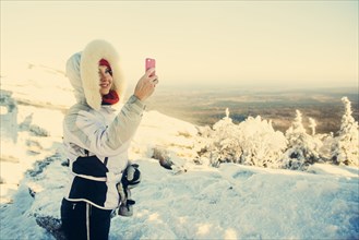 Caucasian hiker taking cell phone photograph in snow