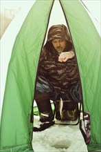 Caucasian hiker ice fishing in tent