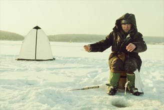 Caucasian man ice fishing on remote lake