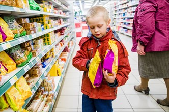 Caucasian boy examining bags of food in grocery store